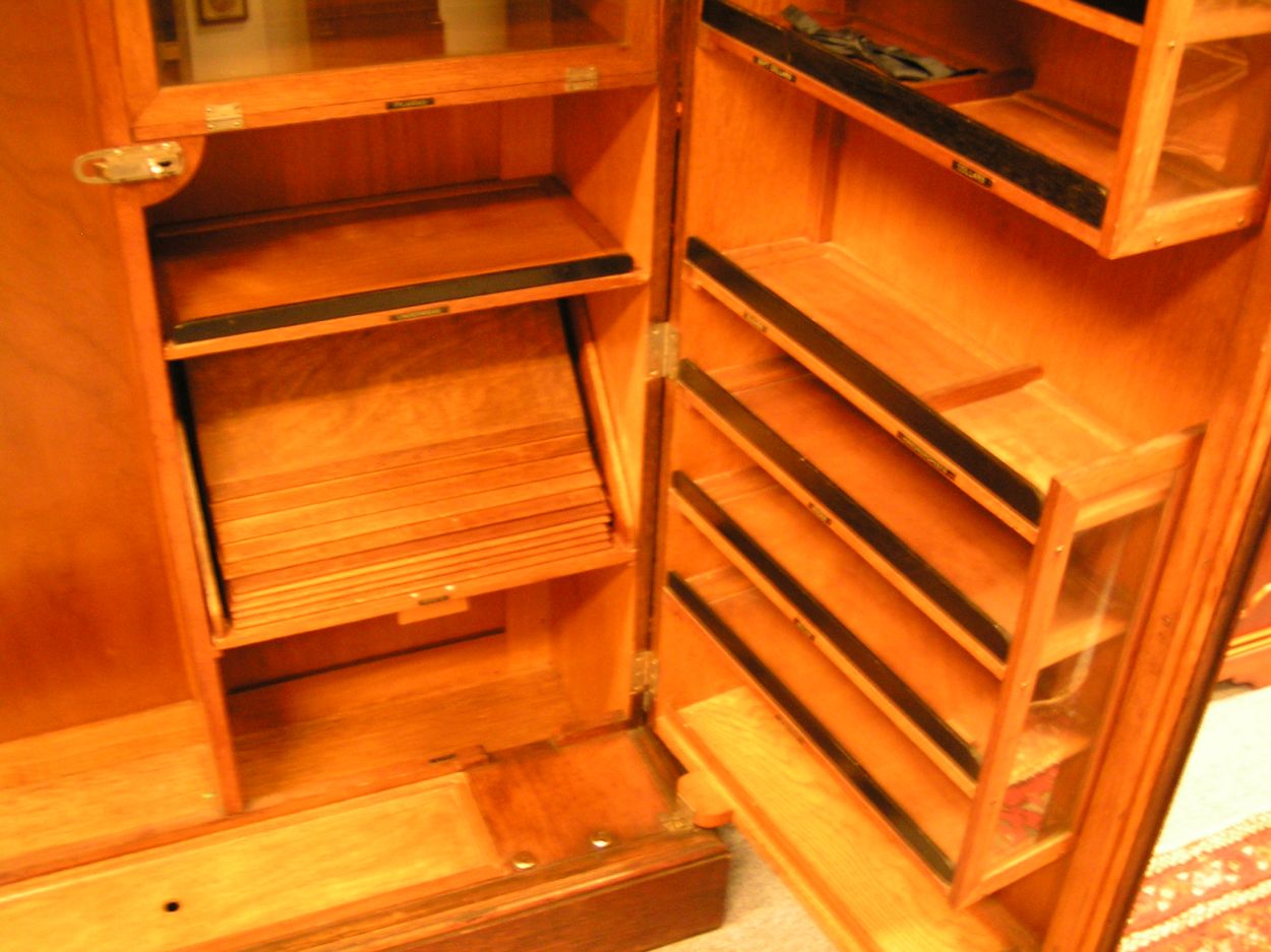 Verkocht 1600240 The Gentlemans Compacton - London:
This piece of furniture is a mystery object. On the outside it looks very ordinary but on the inside it\'s like Aladdin\'s cave.
This Gentleman\'s Compactom resides at Bedervale, a historic home in Braidwood, NSW. The contents of Bedervale is from two families: six generations of the Cogal-Madrel family and the Royds family who moved here in 1973. All the contents that were owned by the Cogal-Madrel family are now owned by the National Trust, gifted by a grant from the National Estate. Bedervale is a living museum.
Victoria, accompanied by her mother Margaret Royds, took me on a tour of the house, sharing with me a few secrets of various objects at Bedervale.
The first object is a Gentleman\'s Compactom.
The Compactom wardrobe - also known as chiffarobe, chifferobe, wardrobe, armoire, dresserobe, closet and Gentleman\'s Butler - demonstrates how an object reflects upon the society that used it. Produced from the 1920s to the 1950s it illustrates how \'designers used wardrobe space to offer the supposed benefits of a tidy and orderly life in a period of rapid change\'. The wardrobe identifies a number of issues including concerns about efficiency, loss of domestic staff, clothes maintenance and middle-class identity\'. Viewed within the context of Bedervale you can see how apparent this was.
During the 1920s Compactoms were often acquired into the marriage when newlyweds started a home together. They were commonly sold as sets with the rest of the bedroom furniture, but could also be purchased individually.
Description:
The moulded cornice above a pair of panelled doors enclosing a well-fitted interior of hooks to the right and shelves and compartments to the left, some with glazed doors and others open, bearing labels reading \'Opera Hats\', \'Pyjamas\' and \'Dress Shirts\' etc., the doors with rails and further shelves, with a lidded compartment for \'Sundries\' in the plinth, 127cm wide x 56cm deep x 174cm high, (50\" wide x 22\" deep x 68.5\" high)
A gentleman\'s mahogany Compactom wardrobe, early 20th Century bearing label to interior reading \'Compactum...41 - 44 Upper Berkely St. London\' and retailer\'s label for \'Finnigans Ltd.\'
Keywords: The Gentlemans Compacton